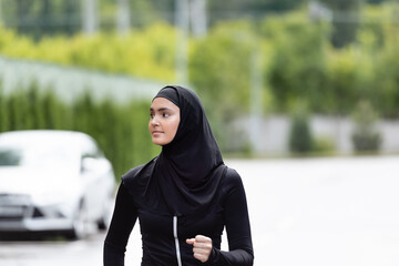 Arabian sportswoman in hijab and sportswear jogging and looking away