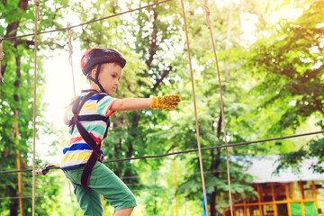 Obraz na płótnie Canvas Little boy passing the cable route high among trees. Kid in safety helmet, extreme sport.