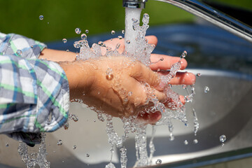 Fototapeta premium Close-up of a little boy washing his hands thoroughly from pollution and protection against germs in a public place, in the park background
