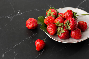 Fresh strawberries in plate on marble black table. Fresh nice strawberries. Strawberry field on fruit farm. Heap of Red strewberry on plate close up. Juice strawberry. Strawberry field on fruit farm.