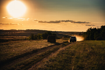At sunset the car is driving on the road and a lot of dust