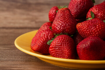 Fresh strawberries in plate on wooden table. Fresh nice strawberries. Strawberry field on fruit farm. Heap of Red strewberry on plate close up. Juice strawberry. Strawberry field on fruit farm.