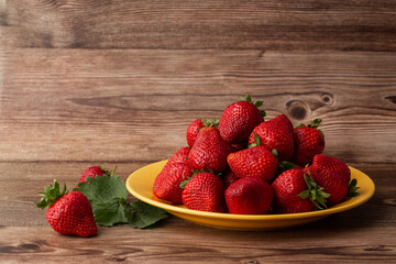 Fresh strawberries in plate on wooden table. Fresh nice strawberries. Strawberry field on fruit farm. Heap of Red strewberry on plate close up. Juice strawberry. Strawberry field on fruit farm.