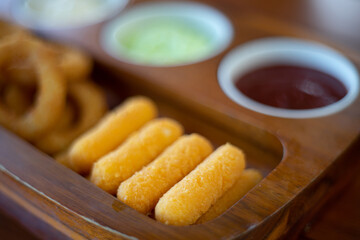 Fried cheese stick onion with sause in wooden tray.