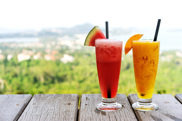 two watermelon and mango smoothies stand on a background of green trees
