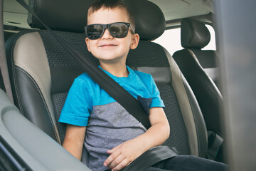 The child is ready for adventures. The boy is sitting in the car in the sunglasses