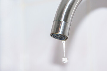 a drop of water drains from the faucet. Fluid leaks and drips downThe concept of lack of drinking water.