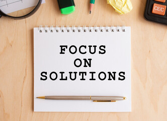 Notepad with text FOCUS ON SOLUTION on a wooden table, near calculator and office supplies. Business concept.