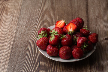 Fresh strawberries in a plate on wooden table. Fresh nice strawberries. Strawberry field on fruit farm. Heap of Red strewberry on plate close up. Juice strawberry. Strawberry field on fruit farm.