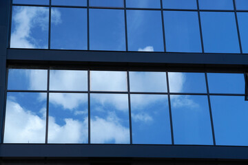 facade of a modern building on a bright Sunny day, blue sky and clouds reflecting in a glass, beautiful exterior of the new building