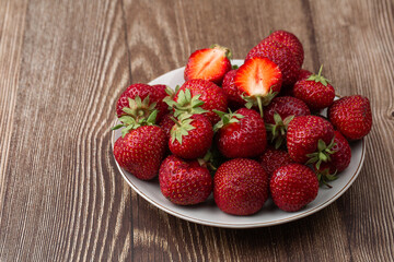Fresh strawberries in a plate on wooden table. Fresh nice strawberries. Strawberry field on fruit farm. Heap of Red strewberry on plate close up. Juice strawberry. Strawberry field on fruit farm.