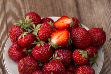 Fresh strawberries in a plate on wooden table. Fresh nice strawberries. Strawberry field on fruit farm. Heap of Red strewberry on plate close up. Juice strawberry. Strawberry field on fruit farm.