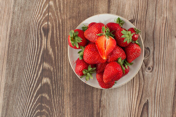 Fresh strawberries in a plate on wooden table. Fresh nice strawberries. Strawberry field on fruit farm. Heap of Red strewberry on plate close up. Juice strawberry. Strawberry field on fruit farm.