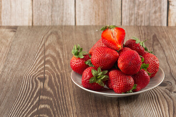 Fresh strawberries in a plate on wooden table. Fresh nice strawberries. Strawberry field on fruit farm. Heap of Red strewberry on plate close up. Juice strawberry. Strawberry field on fruit farm.