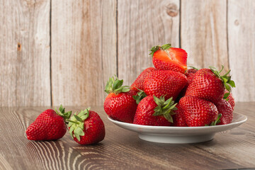 Fresh strawberries in a plate on wooden table. Fresh nice strawberries. Strawberry field on fruit farm. Heap of Red strewberry on plate close up. Juice strawberry. Strawberry field on fruit farm.