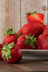 Fresh strawberries in a plate on wooden table. Fresh nice strawberries. Strawberry field on fruit farm. Heap of Red strewberry on plate close up. Juice strawberry. Strawberry field on fruit farm.