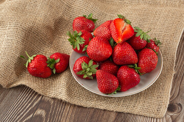 Fresh strawberries in a plate on wooden table. Fresh nice strawberries. Strawberry field on fruit farm. Heap of Red strewberry on plate close up. Juice strawberry. Strawberry field on fruit farm.