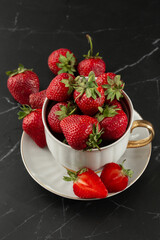 Fresh strawberries in a white cup on marble black table. Fresh nice strawberries. Strawberry field on fruit farm. Heap of Red strewberry on plate. Juice strawberry. Strawberry field on fruit farm.