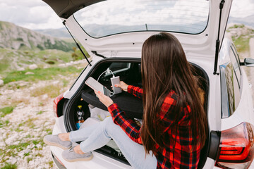 Woman traveler charging smartphone with powerbank in mountains. Pretty female travel by car and using phone and battery charge on vacations in mountains.