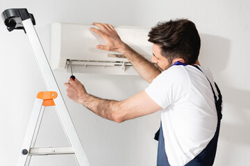 repairman talking on smartphone while fixing air conditioner with screwdriver