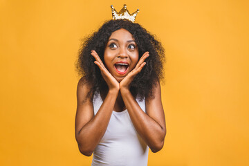 Young african american woman wearing golden crown of queen over isolated over yellow background...