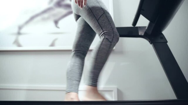 Low angle view of barefoot female in sportwear walking on electric treadmill in medical centre. Young athlete having flat-foot problem, female patient having consultation and physcal training with