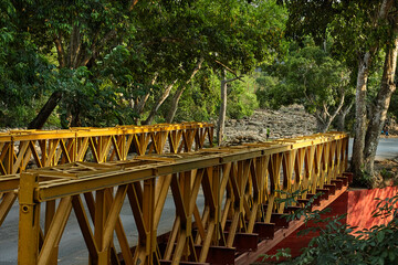 yellow bridge over stony river in tropical landscape