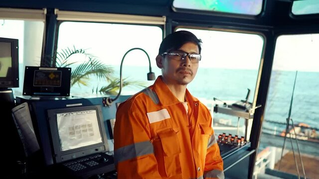 Filipino deck Officer on bridge of vessel or ship wearing coverall during navigaton watch at sea . He is plotting position on chart
