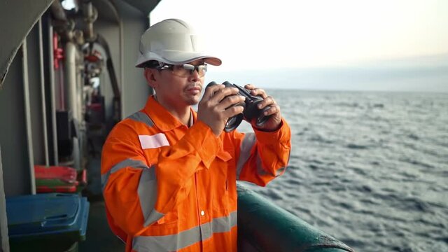Filipino deck Officer on deck of vessel or ship , wearing PPE personal protective equipment. He is looking through binoculars.