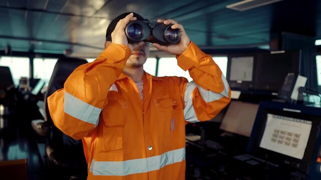 Filipino deck Officer on bridge of vessel or ship wearing coverall. He is looking through binoculars. COLREG navigaton watch at sea