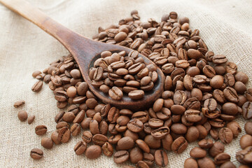coffee beans in a wooden spoon and around it on sack background