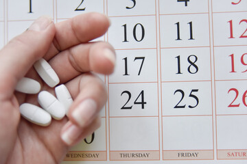 selective focus at pills and calendar with blurry hand