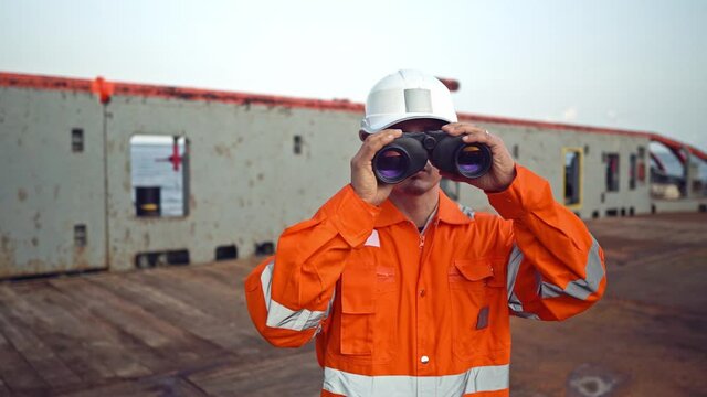 Filipino deck Officer on deck of vessel or ship , wearing PPE personal protective equipment. He is looking through binoculars.