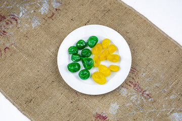 Yellow and green candied kumquat on the white plate on the brown tablecloth.