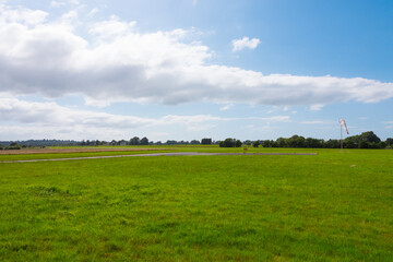 Fototapeta premium Beautiful long shot of a field used as a takeoff/landing runway for planes. Small airdrome in the countryside. Sunny day with no wind as the windsock indicates. 