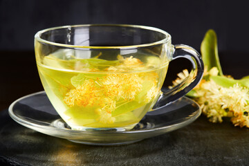 Transparent glass cup of tea with linden on a dark background. 
