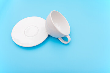 Overturned or  knocked over empty white coffee cup, mug with bowl on blue background, concept picture