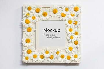 White mockup frame covered with chamomile flowers. Spring and summer concept.