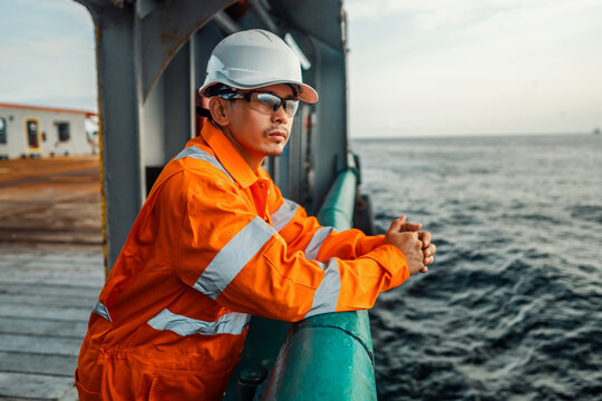 Filipino deck Officer on deck of vessel or ship , wearing PPE personal protective equipment - helmet, coverall, lifejacket, goggles. Safety at sea. He is tired