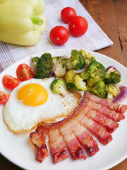 Fried egg with rasher of bacon and broccoli on plate, vertical