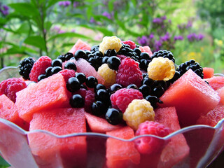 Colorful fruit salad made from garden-grown fruits: watermelon, red and yellow raspberries, and wonderberries (Solanum retroflexum [S. burbankii]) in a clear glass bowl