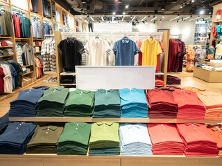 Colorful polo t shirt stack on shelf in large department store shop. Copy space on white sign board.