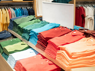 Colorful polo t shirt stack on shelf in large department store shop. Copy space on white sign board.