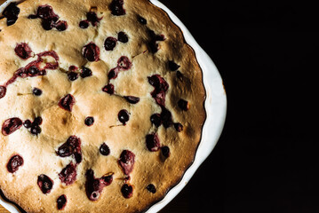cooked homemade pie with berries in a white baking dish on a black background. Homemade sweets, homemade pie, cake 