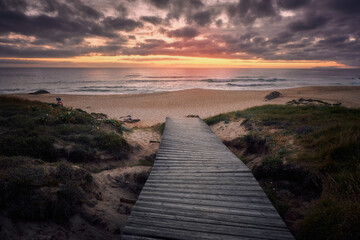 Camino de madera hasta la playa con puesta de sol al fondo