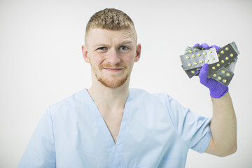 young handsome medical professional disgust grimacing holds many blister pills isolated on white background. Fearful reaction to medication. Addiction on medicines concept