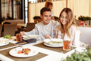 A cheerful and beautiful couple are relaxing on a summer terrace in a restaurant with food and drinks. The guy and the girl have fun on the terrace
