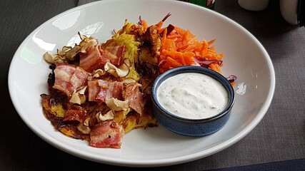 Fried bacon in a pan with carrot salad and white sauce on a plate