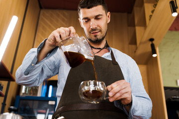Handsome barista pours flavored coffee in glass pot in cafe. Coffee brewing syphon and aeropress alternative methods. Advert for social networks for cafe and restaurant.