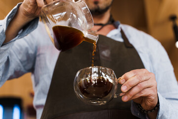 Close-up pouring coffee in double glass cup in cafe by handsome bearded barista. Coffee brewing syphon and aeropress alternative methods. Advert for social networks for cafe and restaurant.